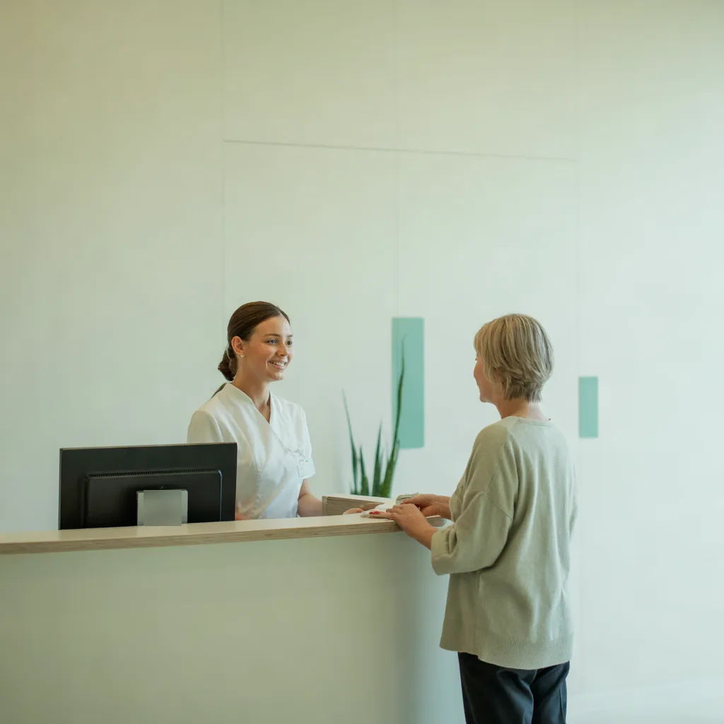 Recepcionista recebe uma paciente no balcão da clínica